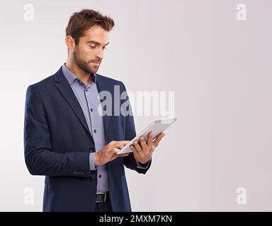 Checking in with the office. Studio shot of a well-dressed man using a tablet against a gray background. Stock Photo