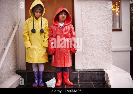 Rain wont interrupt our fun. Portrait of two children dressed in raincoats and wellingtons. Stock Photo