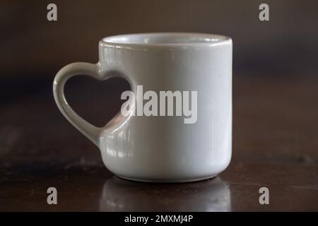 Love in the Morning: A White Mug with Heart Shaped Handle on Wooden Table close up Stock Photo