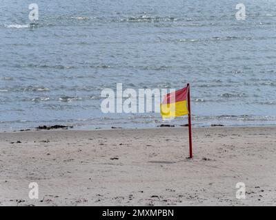 Red and yellow flag allowing swimming on the sandy seashore. Public beach. Stock Photo