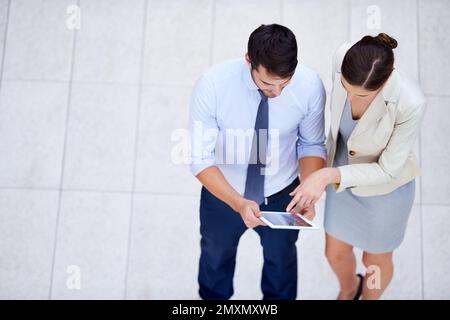 Getting each others input. High angle shot of two business colleagues standing with a digital tablet and discussing work. Stock Photo