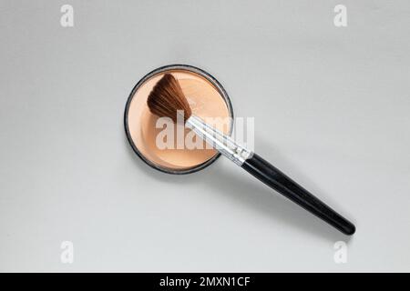 powder in a plastic round package and a brush on a gray background, women's cosmetics close-up, foundation powder Stock Photo