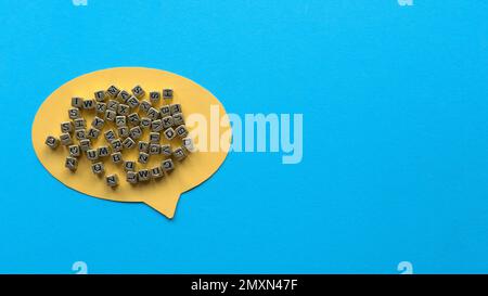 Yellow speech bubble and gold beads of alphabet on blue background with copy space. Stock Photo