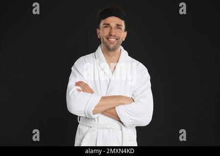 Happy young man in bathrobe and eye sleeping mask on black background Stock Photo