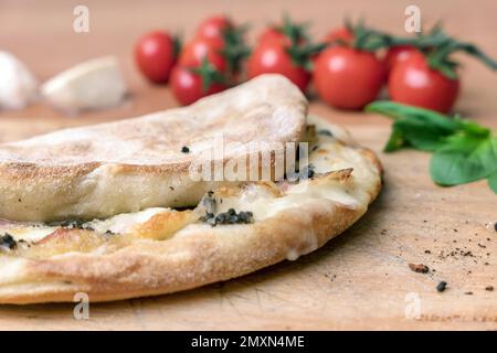 Italian food, closed calzone pizza on rustic wooden background. On blurred background small red tomatoes. Selective focus Stock Photo