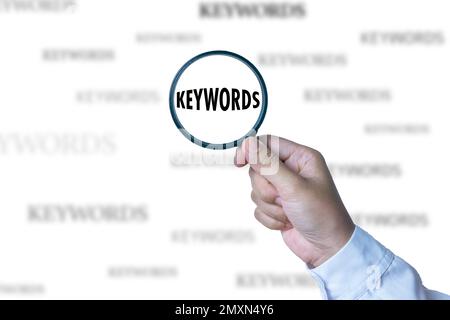 A hand holding a magnifying glass looking for keywords. Stock Photo