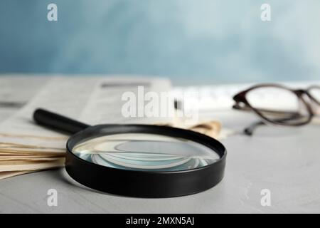 Magnifying glass and stack of newspapers on grey table. Job search concept Stock Photo