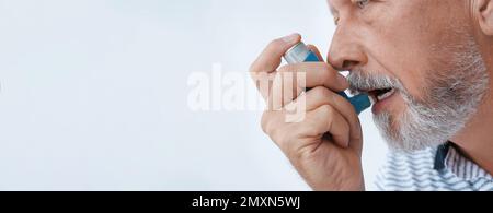 Closeup view of man using asthma inhaler on white background, space for text. Banner design Stock Photo