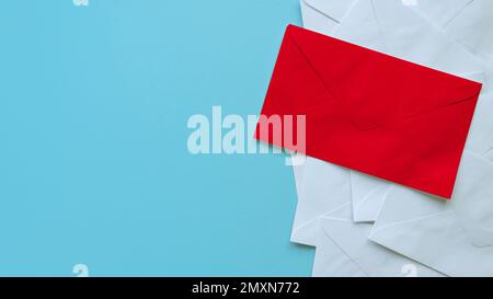 A stack of white envelopes with a red envelope on top. Blue background with copy space. Stock Photo