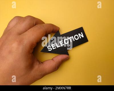 Hand holding arrow wooden board with the word SELECTION on yellow background. Stock Photo