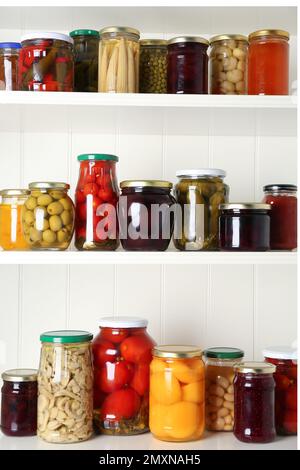 Jars of pickled fruits and vegetables on white wooden shelves Stock Photo