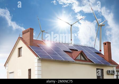 Wind turbines near house with installed solar panels on roof ...