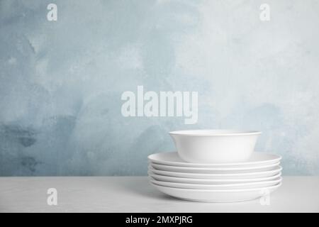 Stack of clean plates and bowl on white table against light blue background. Space for text Stock Photo