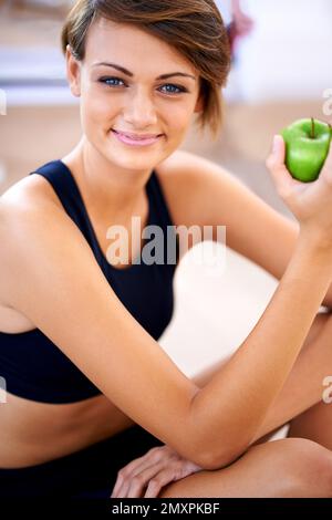 Focussed on a healthy lifestyle. a sporty young woman sitting on a gym floor eating an apple. Stock Photo