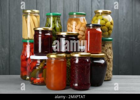Glass jars with different pickled foods on grey wooden background Stock Photo