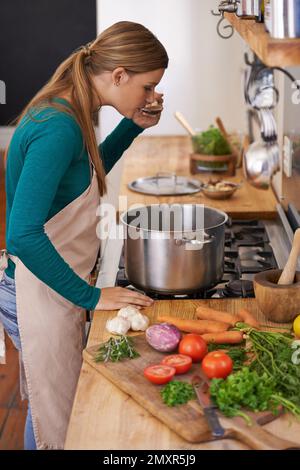 Now thats tasty. a young woman tasting the food she is preparing in the kitchen. Stock Photo