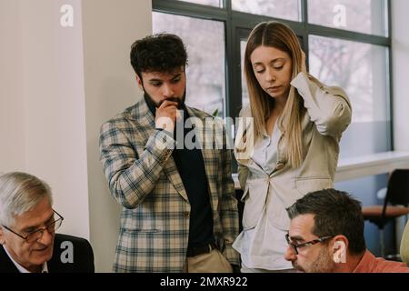 Two senior colleagues talking to each other while their junior coworkers are looking confused at them Stock Photo