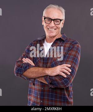 What you see is what you get. Studio portrait of a confident elderly man wearing glasses against a gray background. Stock Photo