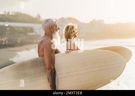 Happy fit surfers with different ages having fun surfing on tropical beach - Extreme sport lifestyle and friendship concept Stock Photo