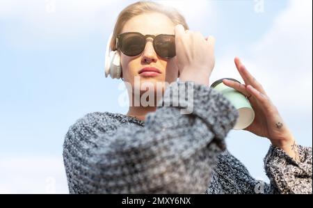 Short hair woman with sunglasses and headphones standing outdoors and looking at camera. Stock Photo
