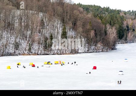 Fishermen fishing on a frozen lake in winter with fishing pole or rod, ice auger, various equipment for fishing and portable thermal tents, aerial Stock Photo