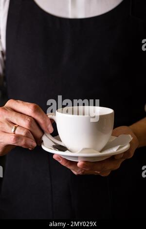 barista in a white shirt and black apron holds a cup of coffee. Stock Photo
