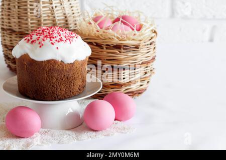 Minimalistic Easter composition with wicker basket with pink colored eggs and Easter cake on white background. Copy space Stock Photo