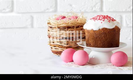 Minimalistic Easter composition with wicker basket with pink colored eggs and Easter cake on white background. Copy space Stock Photo