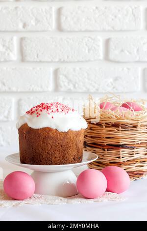 Minimalistic Easter composition with wicker basket with pink colored eggs and Easter cake on white background. Copy space Stock Photo