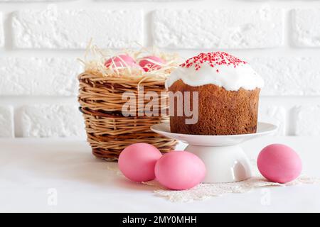 Minimalistic Easter composition with wicker basket with pink colored eggs and Easter cake on white background Stock Photo