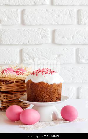 Minimalistic Easter composition with wicker basket with pink colored eggs and Easter cake on white background. Copy space Stock Photo