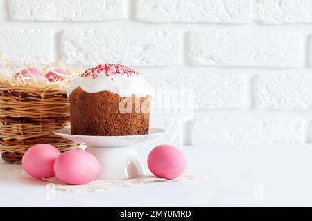 Minimalistic Easter composition with wicker basket with pink colored eggs and Easter cake on white background. Copy space Stock Photo