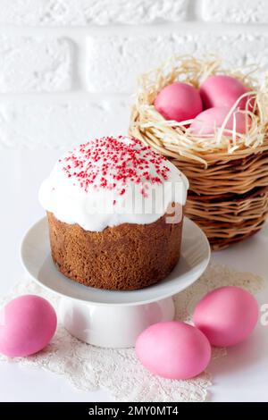 Minimalistic Easter composition with wicker basket with pink colored eggs and Easter cake on white background Stock Photo