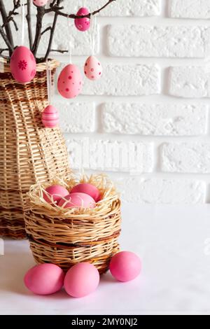 Easter composition with decorated tree branches in a wicker vase and pink colored eggs in wicker basket on white background. Copy space Stock Photo