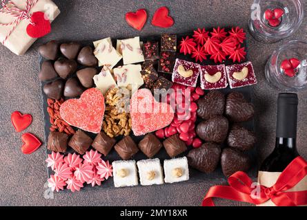 Charcuterie sweet board with different sweets, chocolate, marmalade hearts, nuts and candies as well wine and two glass. Snacks dessert for romantic V Stock Photo