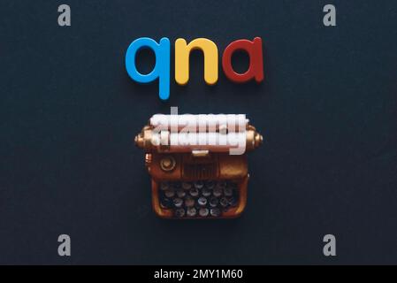 Questions and answers concept. Alphabet qna and miniature typewriter on dark background. Stock Photo