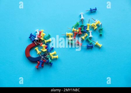 Horseshoe magnet holding a bunch of colorful pins on a blue background. Stock Photo