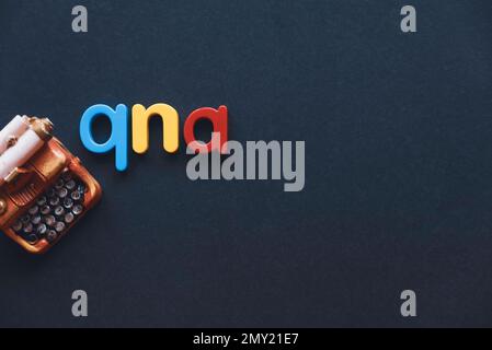 Questions and answers concept. Alphabet qna and miniature typewriter on dark background with copy space. Stock Photo