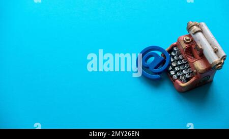 Email icon or symbol with a miniature typewriter on a blue background with copy space. Stock Photo