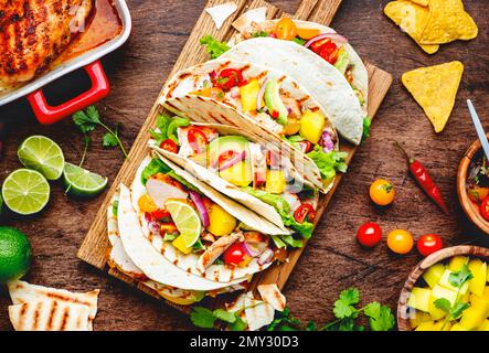 Tacos with grilled chicken, tomato salsa sauce, mango, cilantro and onion in corn tortilla on wooden board. Rustic table background, top view Stock Photo
