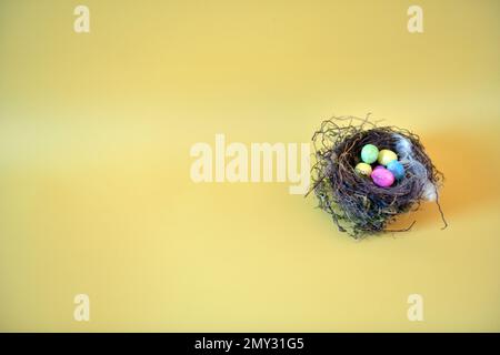 Small bird's nest and artificial eggs on yellow surface.  Copy space to the left. Stock Photo