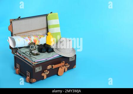 Packed vintage suitcase with clothes on light blue background, space for text. Summer vacation Stock Photo