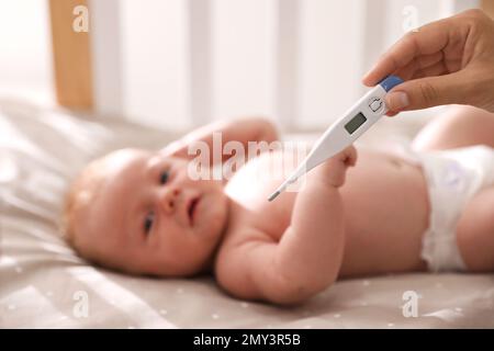 Cute baby lying in crib, focus on woman holding digital thermometer. Health care Stock Photo