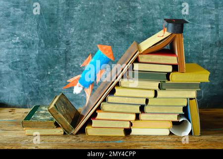 Stack of hardback books with rocketship launching on blackboard background.Learning,education is power,personal development, ladder of sucess and back Stock Photo