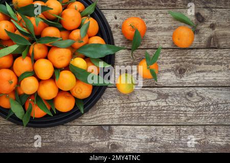 Mandarin oranges with leaves on black tray on wooden background, top table view. Background of fresh tangerines fruit on wooden table with copy space. Stock Photo