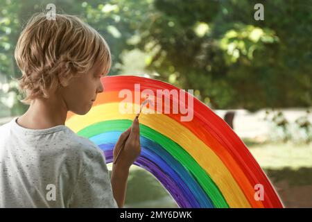 Little boy drawing rainbow on window. Stay at home concept Stock Photo