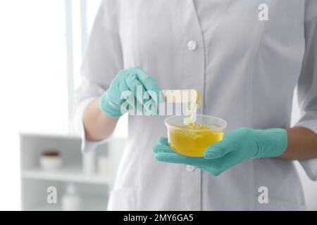 Beautician with bowl of wax and spatula in salon, closeup. Epilation procedure Stock Photo