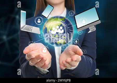 Young businesswoman holding digital image of Earth and different devices in hands on color background, closeup Stock Photo