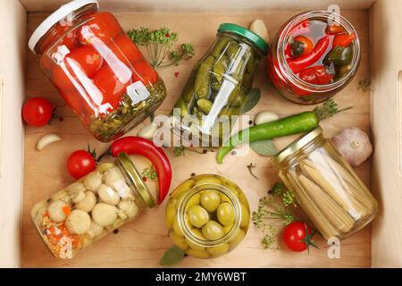 Jars of pickled vegetables in wooden crate, flat lay Stock Photo