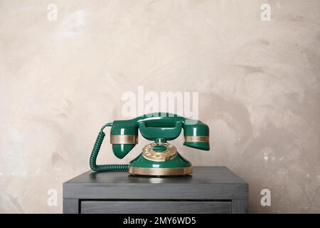 Green vintage corded phone on small black table near beige wall Stock Photo